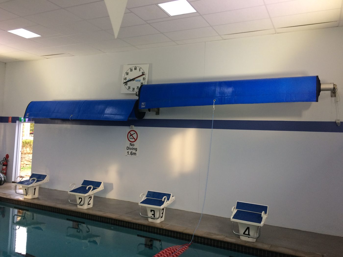 Wall-mounted motorised pool cover winding system above a commercial pool